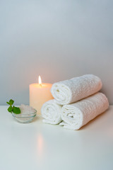 Obraz na płótnie Canvas Wellness and SPA concept photo with white towels stack, candle light, sea salt and mint leaf, vertical orientation.