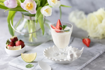 Obraz na płótnie Canvas Panna cotta in glass glasses with strawberries on a light background. Bouquet of tulips on a white table.