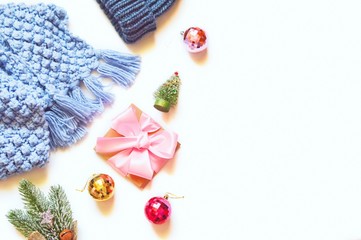  Winter knitted scarf and hat, wrapped gift box with satin bow, decorative green fir tree, red and yellow shiny balls. Flat lay Christmas background. New Year things view from above photography