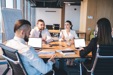 Team of coworkers having discussion and using laptop at meeting in conference room