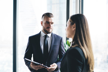 Serious businessman talking to coworker and using tablet while standing in office lobby