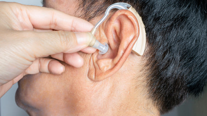 Doctor insert digital hearing aid in senior deft patient ear in hospital,high technological...