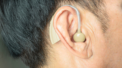 Deaf middle aged man wearing modern digital  hearing aid in ear,high technology of a device...