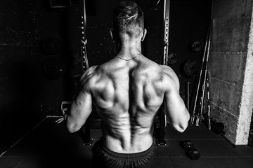 Fototapeta na wymiar Young muscular fit sweaty strong man doing cross workout training for back muscles in the gym dark image real people black and white