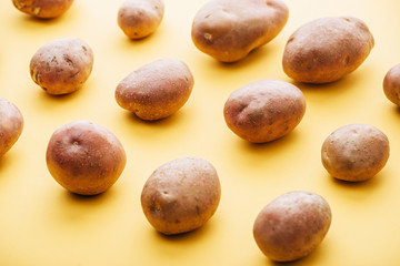 Fototapeta na wymiar pattern of raw whole fresh potatoes on yellow background