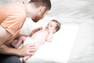 young modern father is caring for his newborn son. Changes the diaper on the bed. Hygiene and...