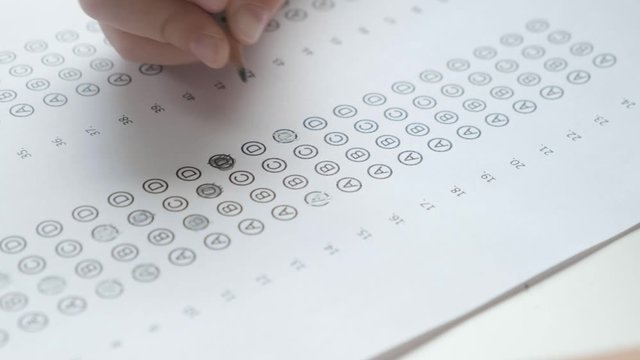 Kid's hand filling bubble test with a pencil, close up. Education and exams concept