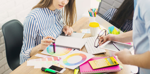 Beautiful young designers discussing ideas and smiling while working in office