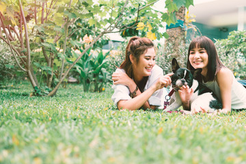 Portrait of happy family in back yard at home, Two young beautiful women with french bulldog lay down on lawn to play with her dog.
