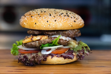 A big fresh colorful burger with meat, egg, salad, onion rings and dips on a wooden tray