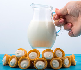 a girl holds a jug of milk over milk cakes in waffle cones