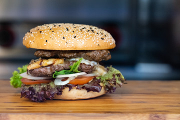 A big fresh colorful burger with meat, egg, salad, onion rings and dips on a wooden tray