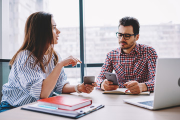 Male and female colleagues talking while share multimedia files via smartphones during working...