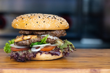 A big fresh colorful burger with meat, egg, salad, onion rings and dips on a wooden tray