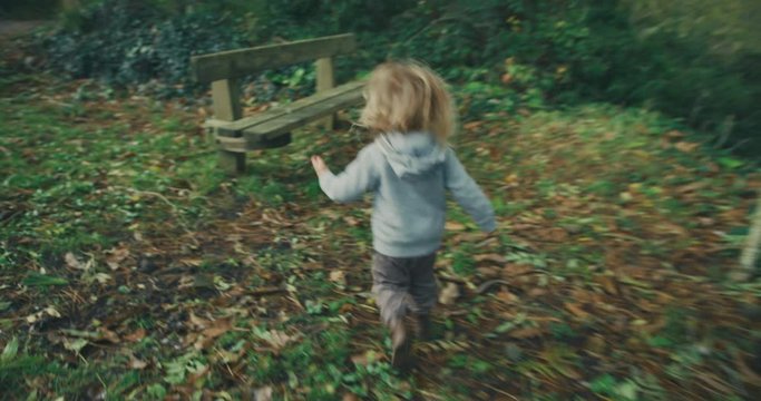 Little toddler running to a bench in woodlands
