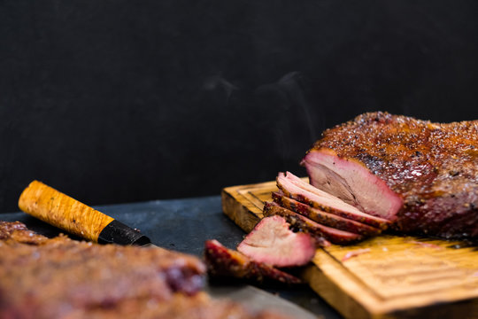 Grill restaurant kitchen. Closeup of sliced hot smoked beef brisket on rustic wooden board. Copy space.