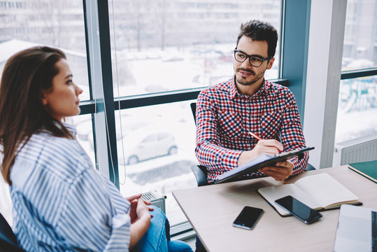 Male employer making notes during conversation on interview with female candidate for job in office,man writing ideas during discussion for common startup with woman employee sitting at desktop .