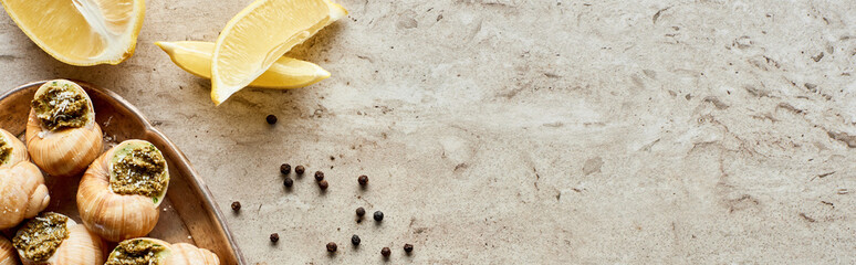 top view of delicious cooked escargots with lemon slices, black peppercorn on stone background,...