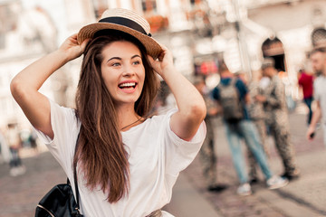 Young stylish woman walking on the old town street, travel with backpack, straw hat, wearing trendy outfit.