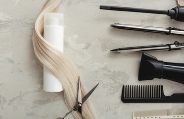 Flat lay composition with Hairdresser tools and white bottle of cosmetic product, blonde hair on gray background. Shampoo mockup. Space for design. Hairdresser service. Natural cosmetics concept.