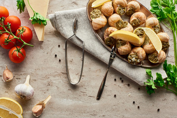 Fototapeta premium top view of delicious served escargots near fresh ingredients on stone background