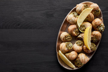 top view of delicious cooked escargots with lemon on black wooden table