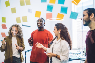 Smiling colleagues arranging sticky notes on glass wall