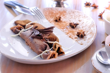 Chocolate russian pancakes, blini with curd filling on the plate. Served with a cup of tea and...