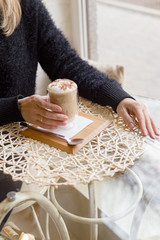 Woman drink Hot latte or Cappuccino coffee in a cafe near window.Latte coffee with milk, chocolate on top in a double-walled glass on a serving board with spoon.Relax, coffee break, breakfast, morning
