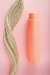 Shampoo for colored hair. Mockup bottle shampoo for blond. Pink bottle of cosmetic product and blonde hair on pink colored background. Space for design. Hairdresser service. Natural cosmetics concept