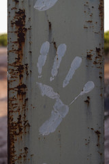 close-up of a silhouette of a hand stamped with white paint on a gray rusty beam