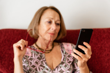 Elegant mature woman using smartphone while sitting on the sofa