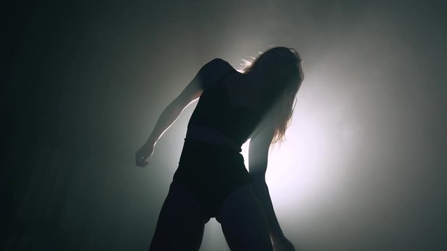 Female silhouette in bright spotlight.Professional dancer moves on stage to music.Plastic girl with sporty and seductive figure.