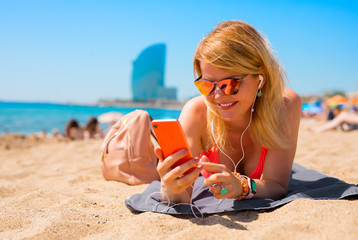 Woman using mobile phone and listening to music while relaxing on the beach