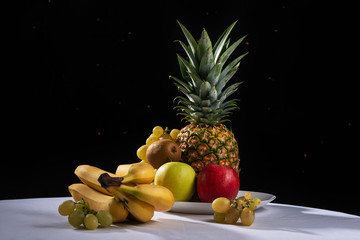 Fruit still life on a black festive background, pineapple, grapes, apples, kiwi, citrus.