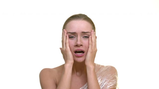 Close up of lady expressing anxiety on isolated white background. Troubled attractive woman touches her face with both hands with depressed mock up gesture inside a studio 