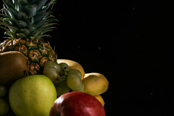 Fruit still life on a black festive background, pineapple, grapes, apples, kiwi, citrus.