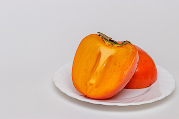 Orange persimmon cut into two halves on a white plate, on a white background. A great choice for a...