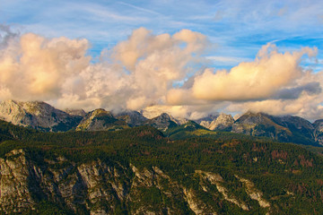 Picturesque view of high mountain landscape during sunset. Some mountain peaks are covered with thick white clouds which backlit by the sun. Concept of landscape and nature. Slovenia
