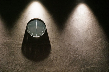 Black simple analog clock showing midnight hanging on the wall with shadows and copy space on the...