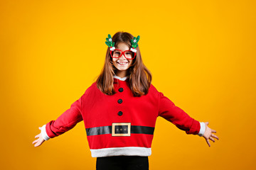 Studio shot of beautiful little girl wearing santa claus hoodie suit, posing over yellow isolated background. Christmas & new year themed portrait of female smiling. Close up, copy space, background.