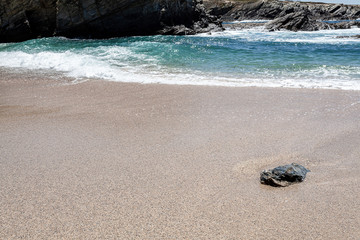 Pedra isolada na areia da praia na zona de rebentação das ondas.