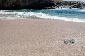 Pedra isolada na areia da praia na zona de rebentação das ondas.