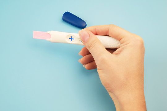Closeup of a woman's hand with a positive pregnancy test on a blue background.