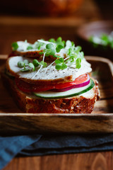 Sandwich with turkey breast and fresh vegetables served with microgreens on a wooden plate. The concept of healthy and diet eating.