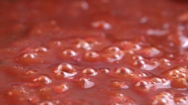Hot tomato sauce is heated and boiled in a pan, cooking in slow motion side view
