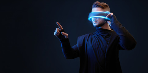 Model young man with beard in glasses of virtual reality on dark background. Augmented reality, future technology concept. VR. Blue neon light. © KDdesignphoto