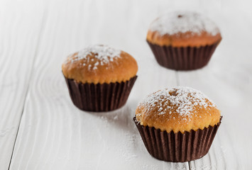 Tasty cupcake with icing sugar on a wooden table.