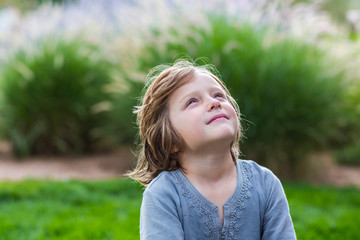 Young boy sitting on green lawn and looking up