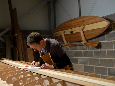 Man using small metal ruler while making wooden paddleboard